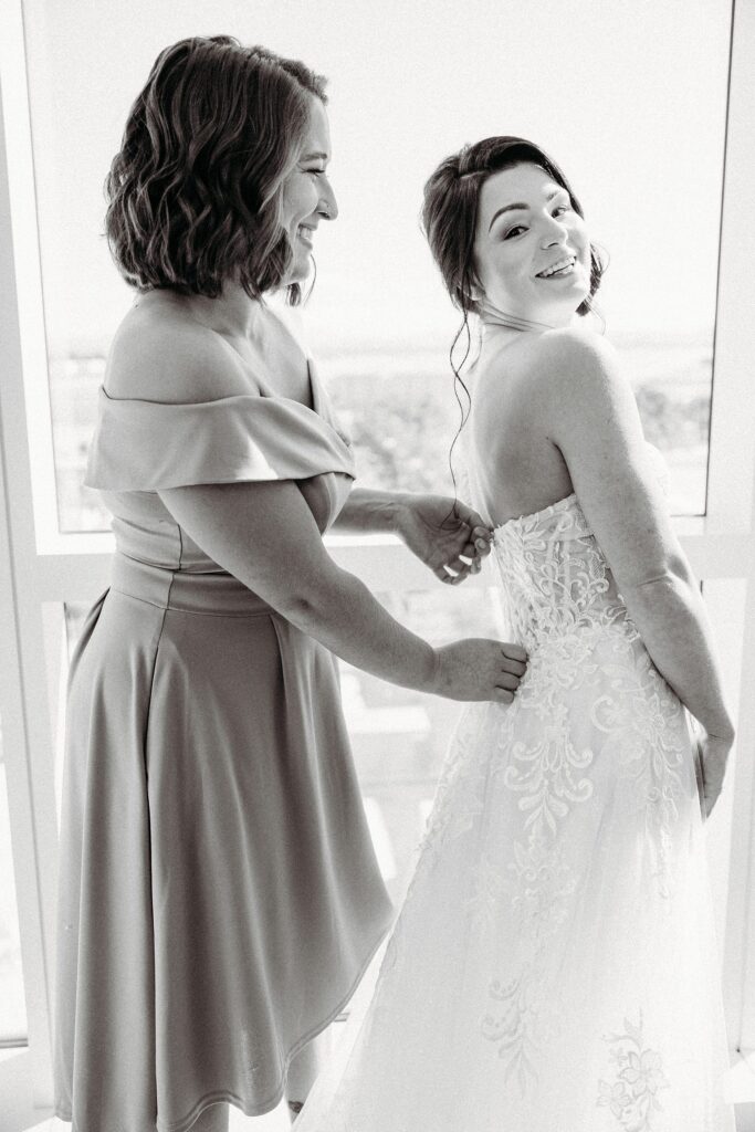 Black and white photo of a bride getting her dress zipped up